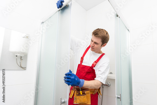 Young man repairing door of shower cabin in bathroom.