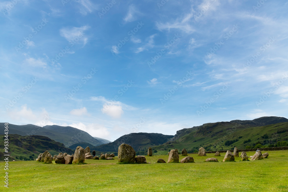 Obraz premium English Heritage Castlerigg Stone Circle of 5000 years old near Keswick, UK in the Lake District National Park on a hill overlooking surrouning hills and mountains against a white clouded blue sky