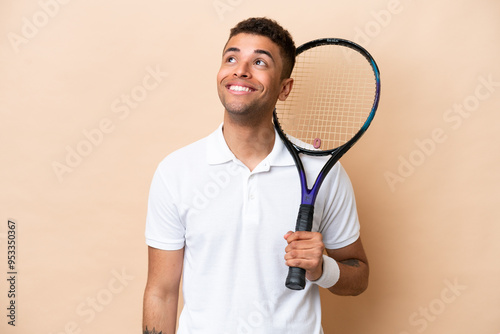 Young brazilian handsome man playing tennis isolated on beige background thinking an idea while looking up photo