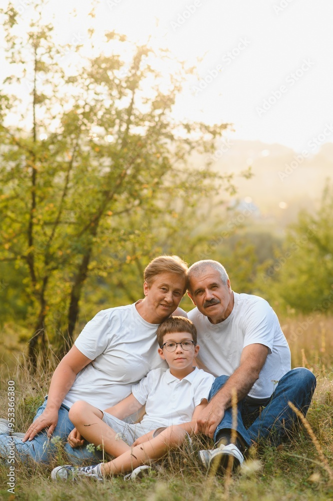 Grandson, grandfather and grandmother sitting on grass having fun outdoors in park at sunset Grandson, grandfather and grandmother sitting on grass having fun outdoors in park at sunset