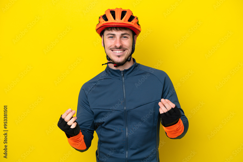 Young cyclist caucasian man isolated on yellow background making money gesture Young cyclist caucasian man isolated on yellow background making money gesture