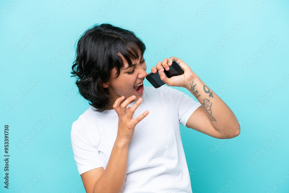 Young Argentinian woman isolated on blue background using mobile phone and singing Young Argentinian woman isolated on blue background using mobile phone and singing
