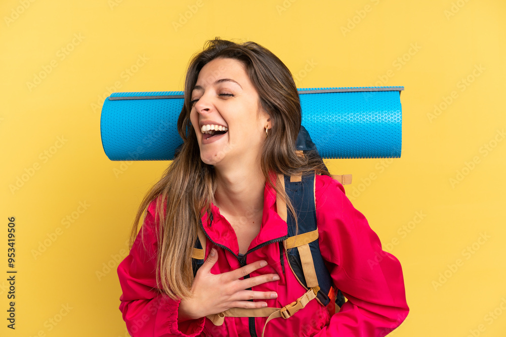 Young mountaineer man with a big backpack isolated on yellow background smiling a lot Young mountaineer man with a big backpack isolated on yellow background smiling a lot