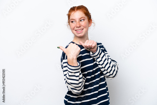 Young reddish woman isolated on white background pointing to the side to present a product