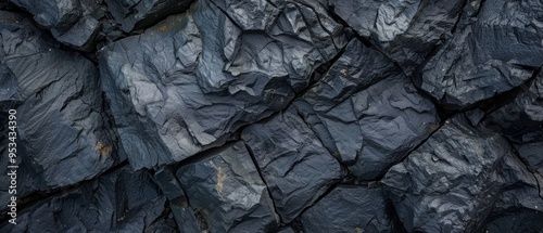 Close-up photo of textured dark rock formation with visible cracks, jagged layers, and weathering. Overcast lighting highlights yellow sediment deposits.