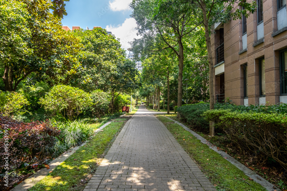 A pavement pedestrian footpath or walkway in a landscaped public garden within residential apartment blocks in a Chinese urban community, lush green trees and shrubs providing shade along walkway A pavement pedestrian footpath or walkway in a landscaped public garden within residential apartment blocks in a Chinese urban community, lush green trees and shrubs providing shade along walkway