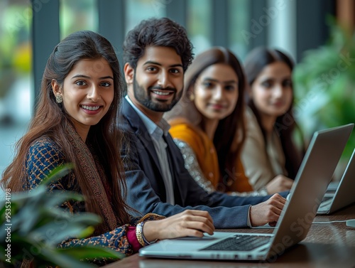 A diverse group of young professionals collaborating in a bright workspace with laptops, focused on productivity and teamwork.