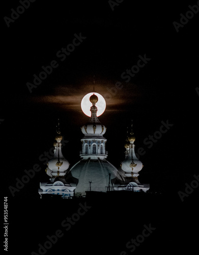 
Close-up of a large round moon setting behind the spire of an Orthodox cathedral