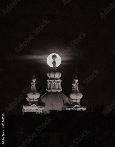 
Close-up of a large round moon setting behind the spire of an Orthodox cathedral
