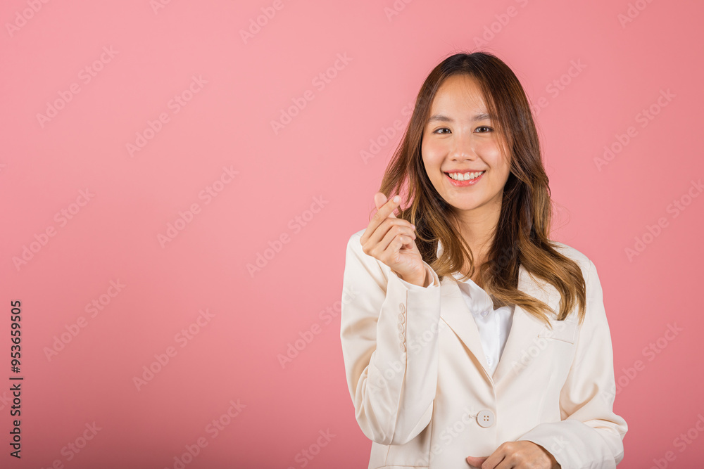 Confident business woman stands with a smile, creating a mini heart sign with her finger on a pink background. Asian portrait of a beautiful young female sending love for Valentine's Day, studio shot Confident business woman stands with a smile, creating a mini heart sign with her finger on a pink background. Asian portrait of a beautiful young female sending love for Valentine's Day, studio shot