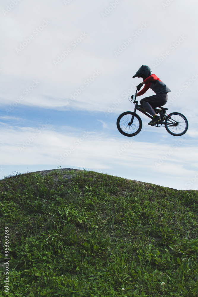Side view of a silhouetted bmx racer flying in the air over a hill of grass. Side view of a silhouetted bmx racer flying in the air over a hill of grass.