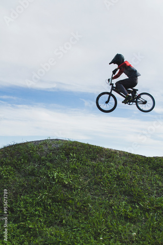 Side view of a silhouetted bmx racer flying in the air over a hill of grass.