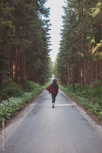 Young woman in a red plaid shirt walking down a peaceful, tree-lined forest road, embracing the tranquility and beauty of nature, symbolizing freedom and a journey of self-discovery