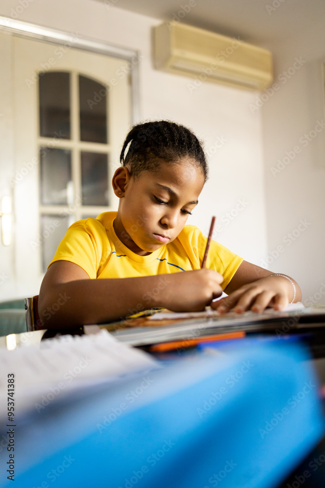 Vertical photo of a dark-skinned boy between 8 and 9 years old writes on the living room table of his house. The young African studies at home. Concept of education for African American children.