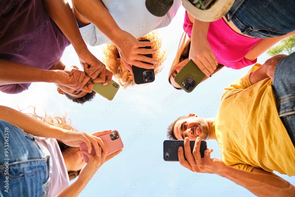 Low angle view of young group of friends in circle using smart mobile phones outdoors.