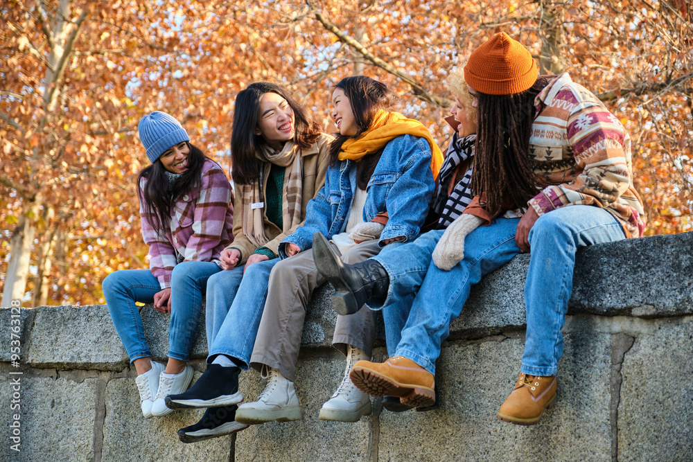 Happy multi-ethnic group of young hipster diverse student friends having fun while hanging out sitting together outdoors. Friendship concept.