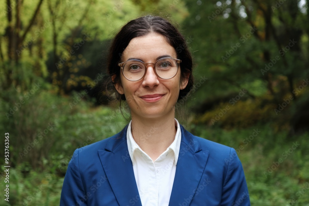 Woman smiling outdoors. Smiling woman wearing glasses and a blue jacket in a natural setting. Woman smiling outdoors. Smiling woman wearing glasses and a blue jacket in a natural setting.