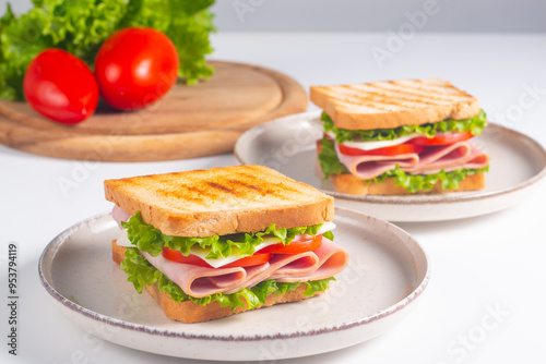 Close-up of two sandwiches with bacon, salami, prosciutto and fresh vegetables on rustic wooden cutting board. Club sandwich concept