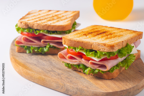 Close-up of two sandwiches with bacon, salami, prosciutto and fresh vegetables on rustic wooden cutting board. Club sandwich concept