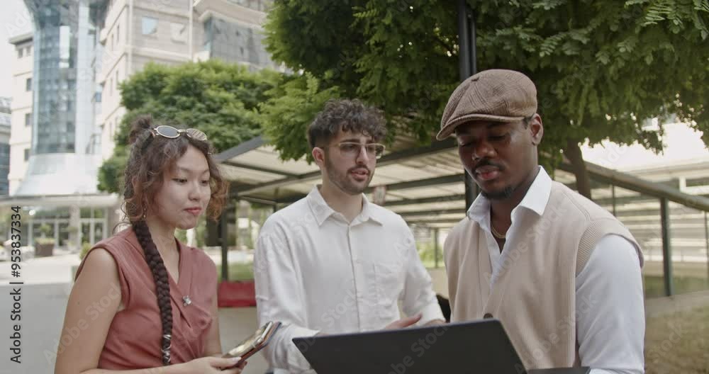 Outdoors, a diverse group of young professionals engages in discussion with a laptop, highlighting their focus on teamwork, collaboration, and contemporary business communication methods. Outdoors, a diverse group of young professionals engages in discussion with a laptop, highlighting their focus on teamwork, collaboration, and contemporary business communication methods.