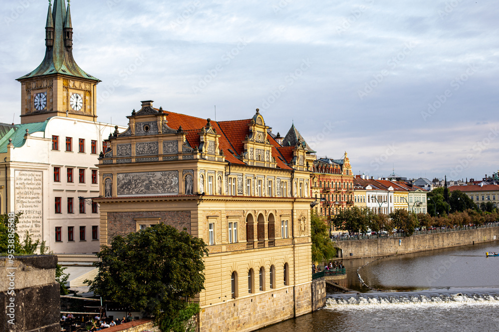 Naklejka premium Historic architecture along the riverbank in Prague at sunset, showcasing stunning buildings and serene water reflections