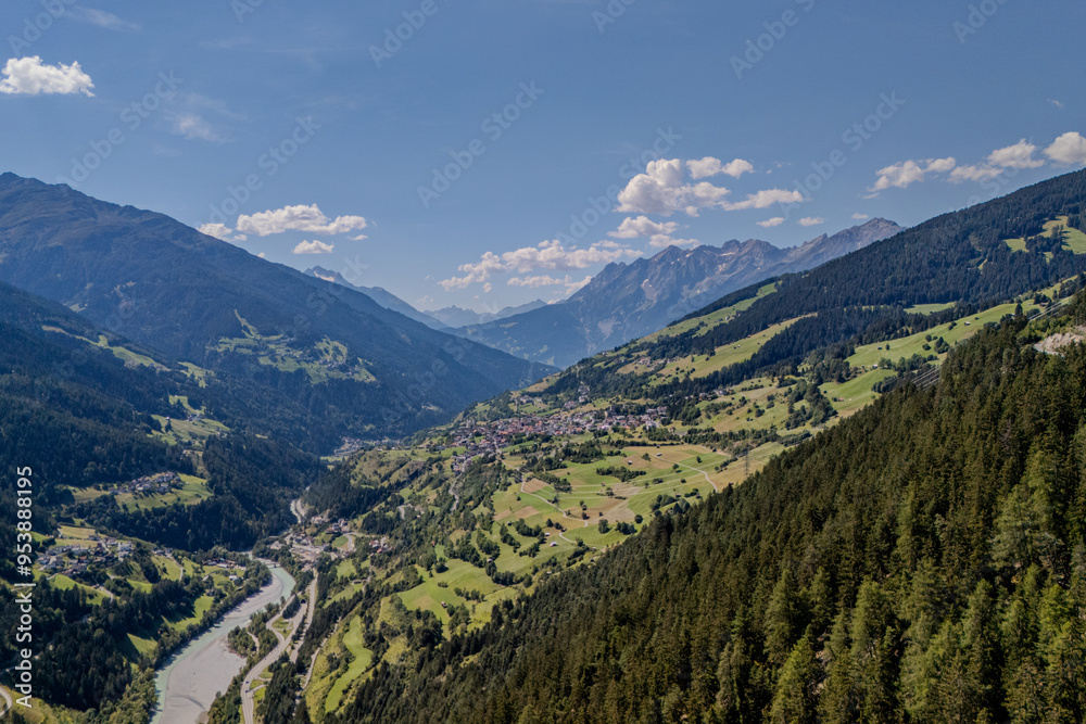 Breathtaking view of a lush valley surrounded by mountains and a winding river under a clear blue sky during summer