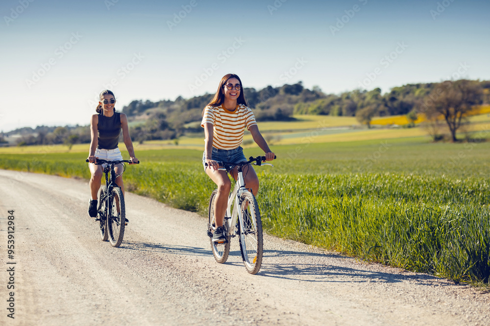 Naklejka premium Young women friends cycling while clapping their hands through rapessed field