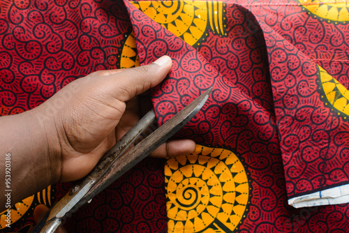 top view of cutting red and yellow ankara fabric with scissors , flatlay of nigerian wax cloth, rumpled red and yellow ankara material photo