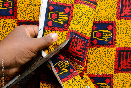 top view of cutting red and yellow ankara fabric with scissors , flatlay of nigerian wax cloth, rumpled red and yellow ankara material photo