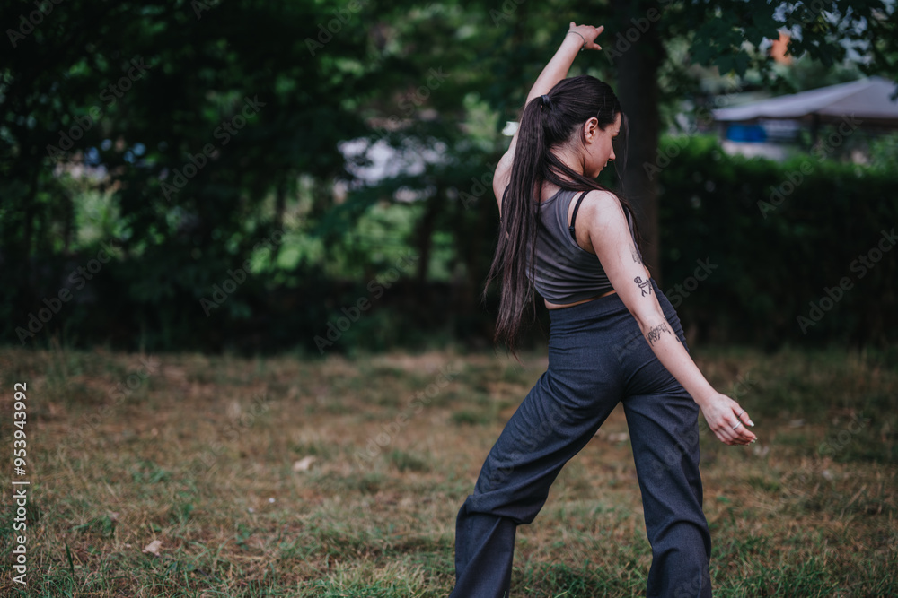 Naklejka premium A young woman embodies freedom and self-expression as she dances gracefully in a lush outdoor park setting.