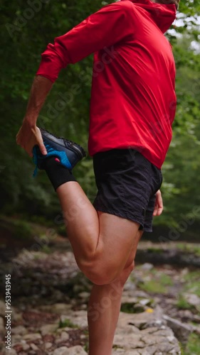 Unrecognisable young man stretching quadricep muscle in the forest. Athlete warming up in nature.