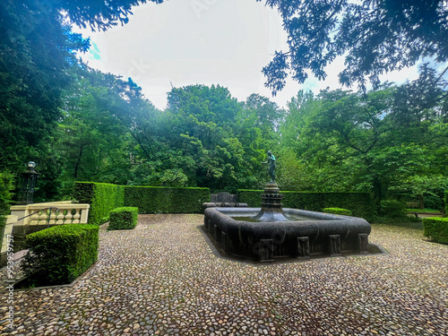 A Garden of a castle or a herrenhausen garden with a fountain in the the middle of it and a lot of green around it. photo