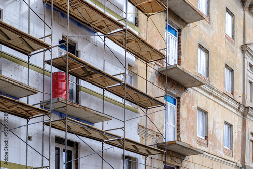 Building facade under renovation works with construction scaffolding frame. Wall insulation with styrofoam sheets for energy efficient home