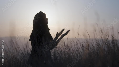 Muslim woman with a veil sitting on ground praying outdoors