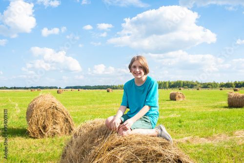 boy sitting on a hay bale in the field with blue sky 