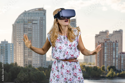 Portrait of amazed blonde woman in vr headset. Residential area buildings in the background. photo