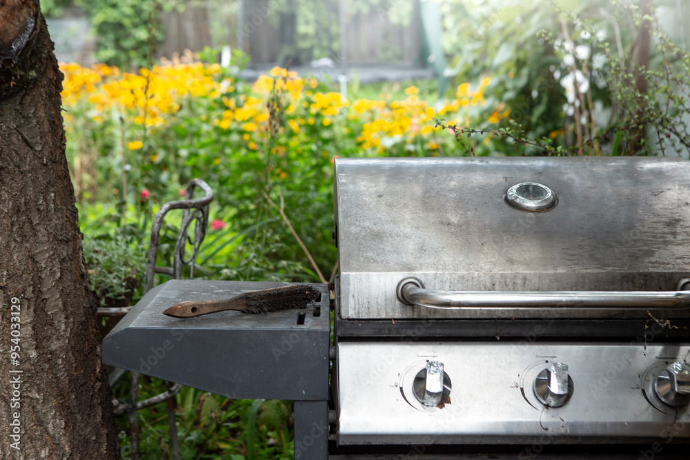 Steel gas burner grill with a garden full of yellow flowers defocused in the background Steel gas burner grill with a garden full of yellow flowers defocused in the background