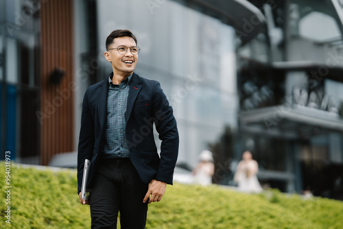 Canvastavla Confident Businessman:  A young, professional Asian man in a suit, carrying a laptop, walks confidently towards a modern office building