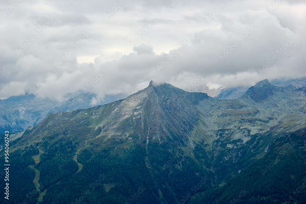 View of an amazing mountain landscape on a hazy day with gray clouds and fog over the peaks in autumn in Austria. View of an amazing mountain landscape on a hazy day with gray clouds and fog over the peaks in autumn in Austria.