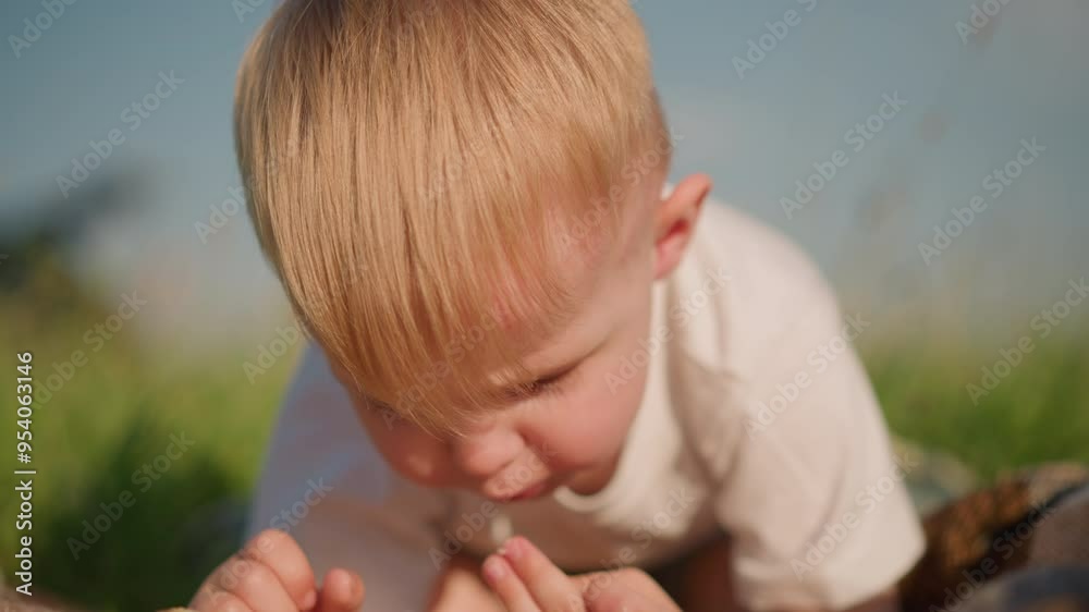 A close-up image of a little boy in a white shirt, bent over, deeply focused on eating a piece of bread. The background is blurred, grassy environment that highlights the peaceful outdoor moment A close-up image of a little boy in a white shirt, bent over, deeply focused on eating a piece of bread. The background is blurred, grassy environment that highlights the peaceful outdoor moment