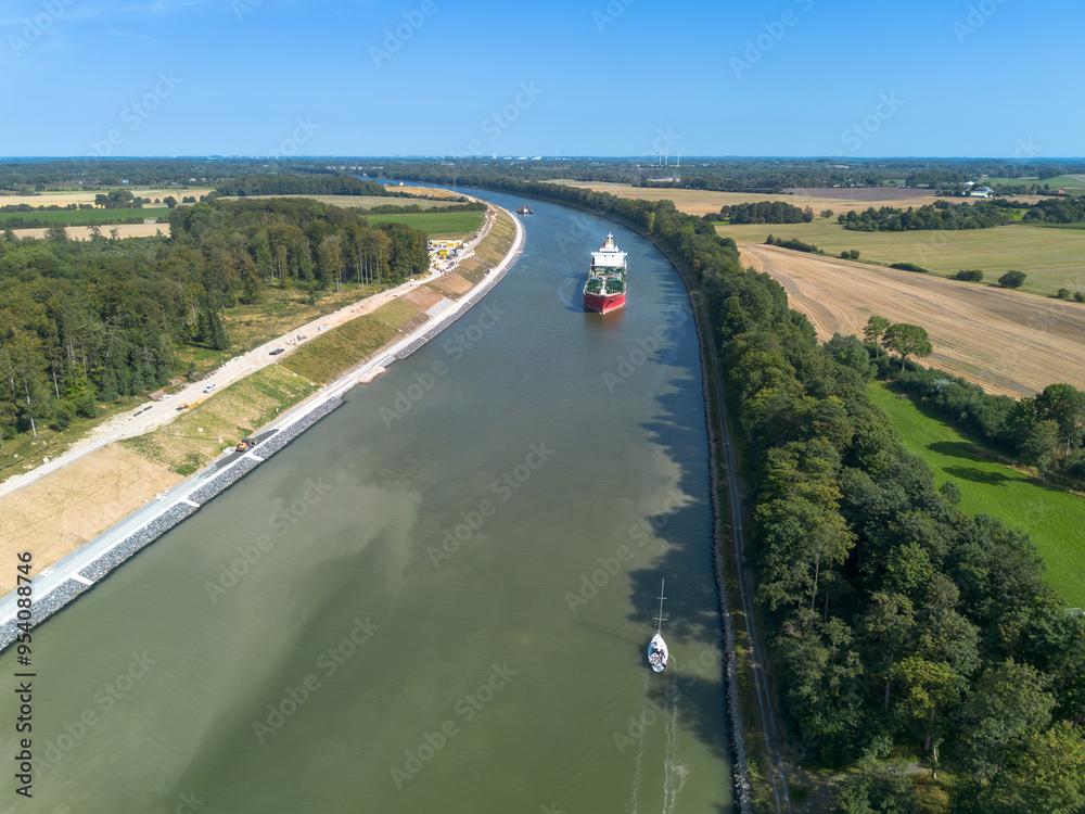 Aerial drone image of the Kiel canal, nord ostsee kanal, in Germany. Blue sky and green bank of the channel, river connecting North Sea and Baltic Sea. Cargo bulk ships and sailboat on water Aerial drone image of the Kiel canal, nord ostsee kanal, in Germany. Blue sky and green bank of the channel, river connecting North Sea and Baltic Sea. Cargo bulk ships and sailboat on water
