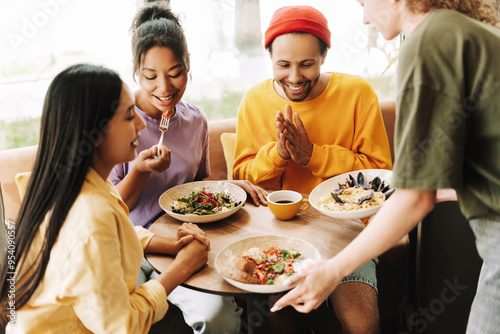 Waitress bringing food to diverse group of friends eating in restaurant photo