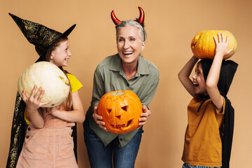 Happy grandmother and two little girls wearing halloween costumes holding pumpkins and smiling