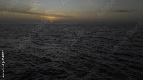 Drone flies toward a fading sunset over choppy waters