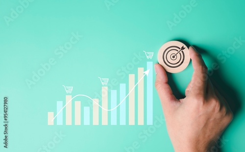 Obraz na płótnie A hand holding a wooden with a target icon, goal achievement or strategic planning, chart and shopping cart icons business growth, an upward trending line indicating positive financial performance. w salonie