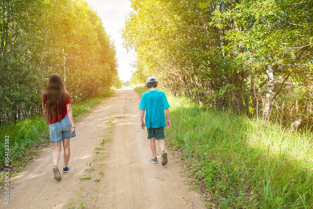 Fototapeta premium Back view of a boy and girl walking on a dirt road in the forest