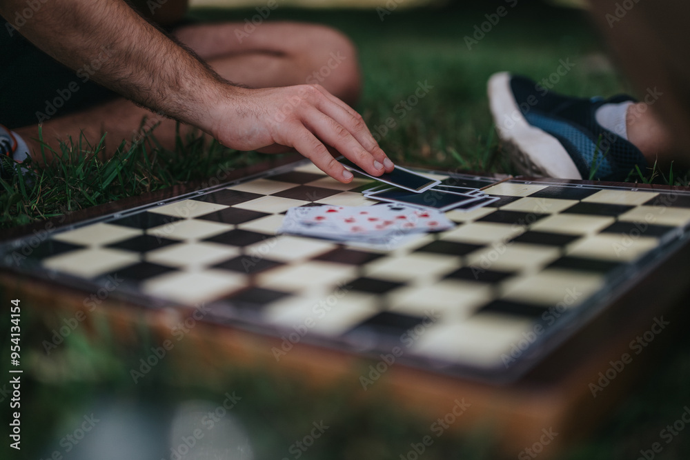 Close-up of a chessboard with playing cards and hand outdoors Close-up of a chessboard with playing cards and hand outdoors