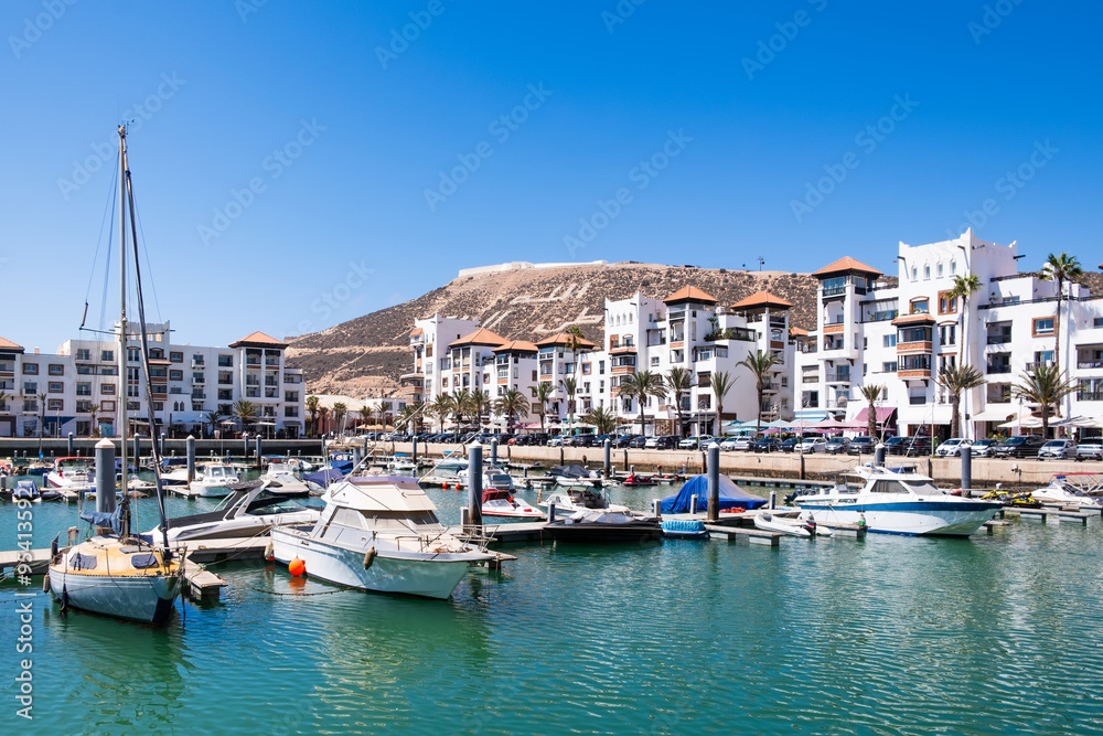 Seaside view of Agadir Marina in Morocco. Popular tourist area with luxury apartments, boats in harbor, shops and restaurants. Moroccan seaside resort on shore of Atlantic ocean in Africa Seaside view of Agadir Marina in Morocco. Popular tourist area with luxury apartments, boats in harbor, shops and restaurants. Moroccan seaside resort on shore of Atlantic ocean in Africa