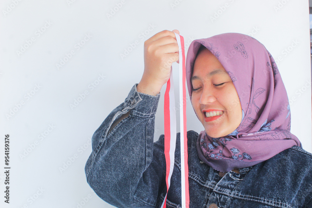 a woman in a purple hijab feels happy while holding a small and long red and white flag. The red and white flag is the national flag of Indonesia. a woman in a purple hijab feels happy while holding a small and long red and white flag. The red and white flag is the national flag of Indonesia.