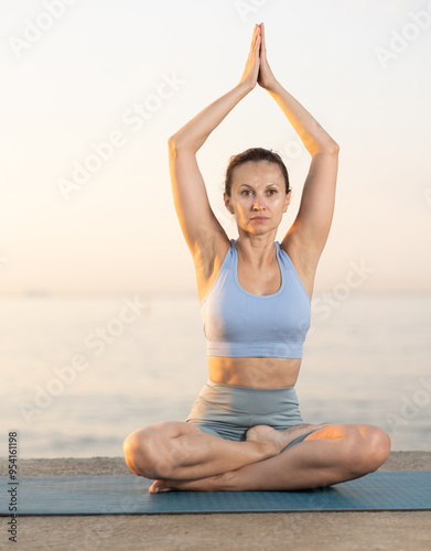 Example of performing hatha yoga asana. Amateur and professional girl does yoga near sea, during sunset in evening she fulfil performs padmasana lotus pose